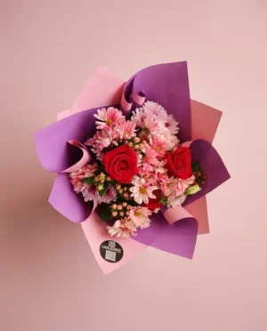 Ramo de rosas rojas y malibú envuelto en papel lila y rosa
