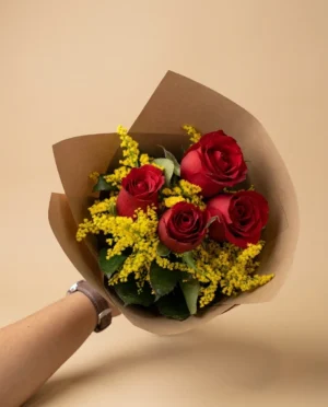 Ramo de rosas rojas con vara de oro y envoltura de papel kraft sostenido en mano